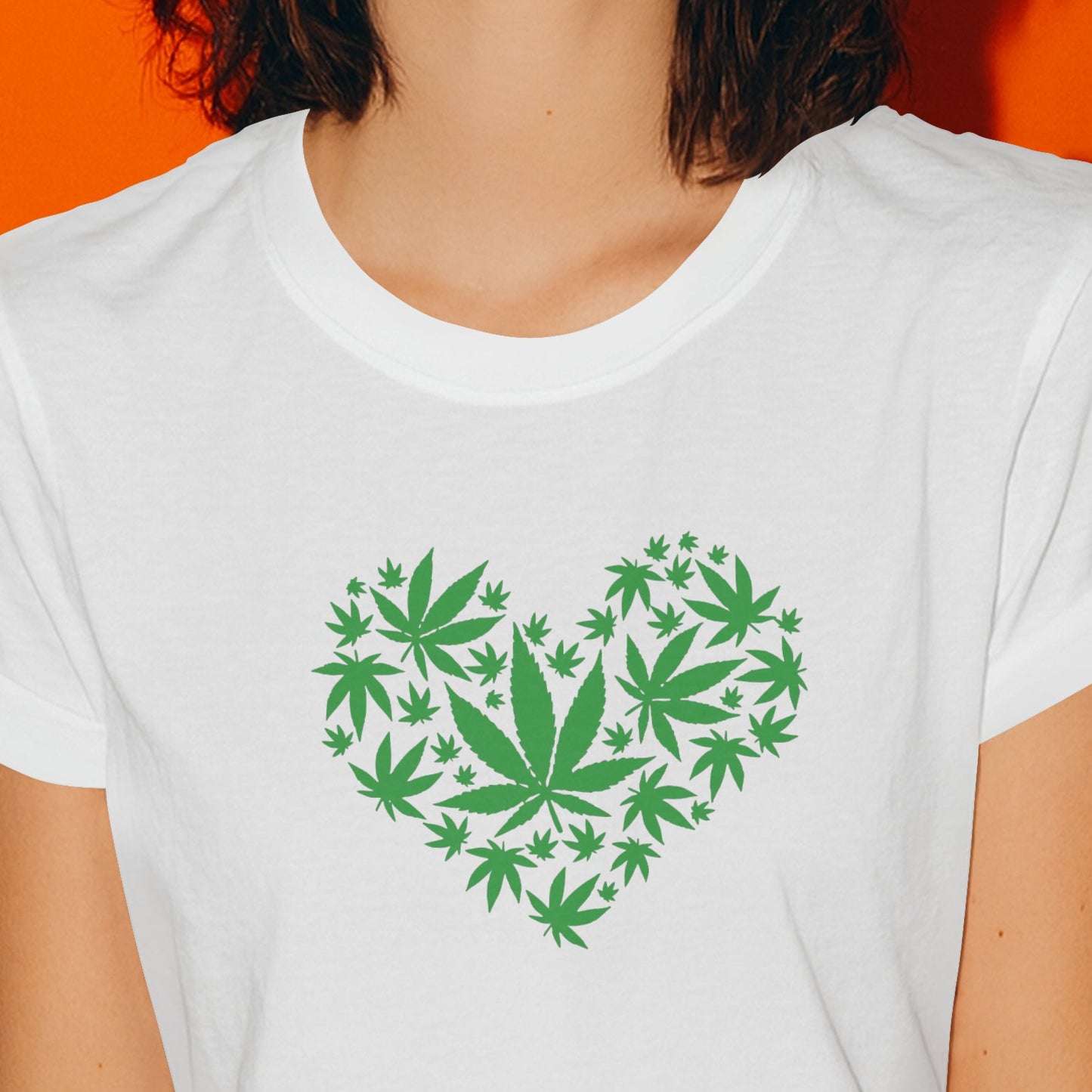 Woman wearing a white t-shirt with a green cannabis leaf design on an orange background