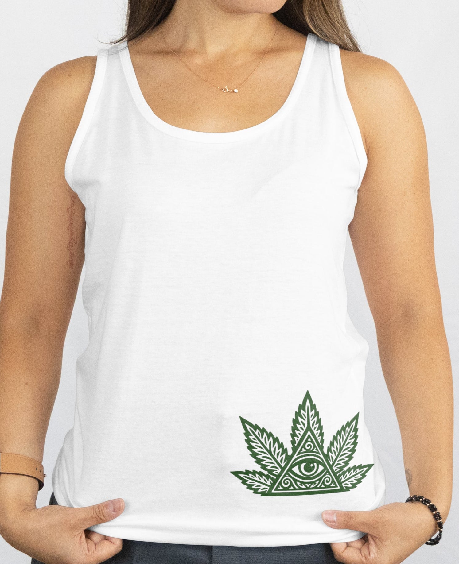 Woman wearing a white tank top with a green cannabis leaf design on a plain background