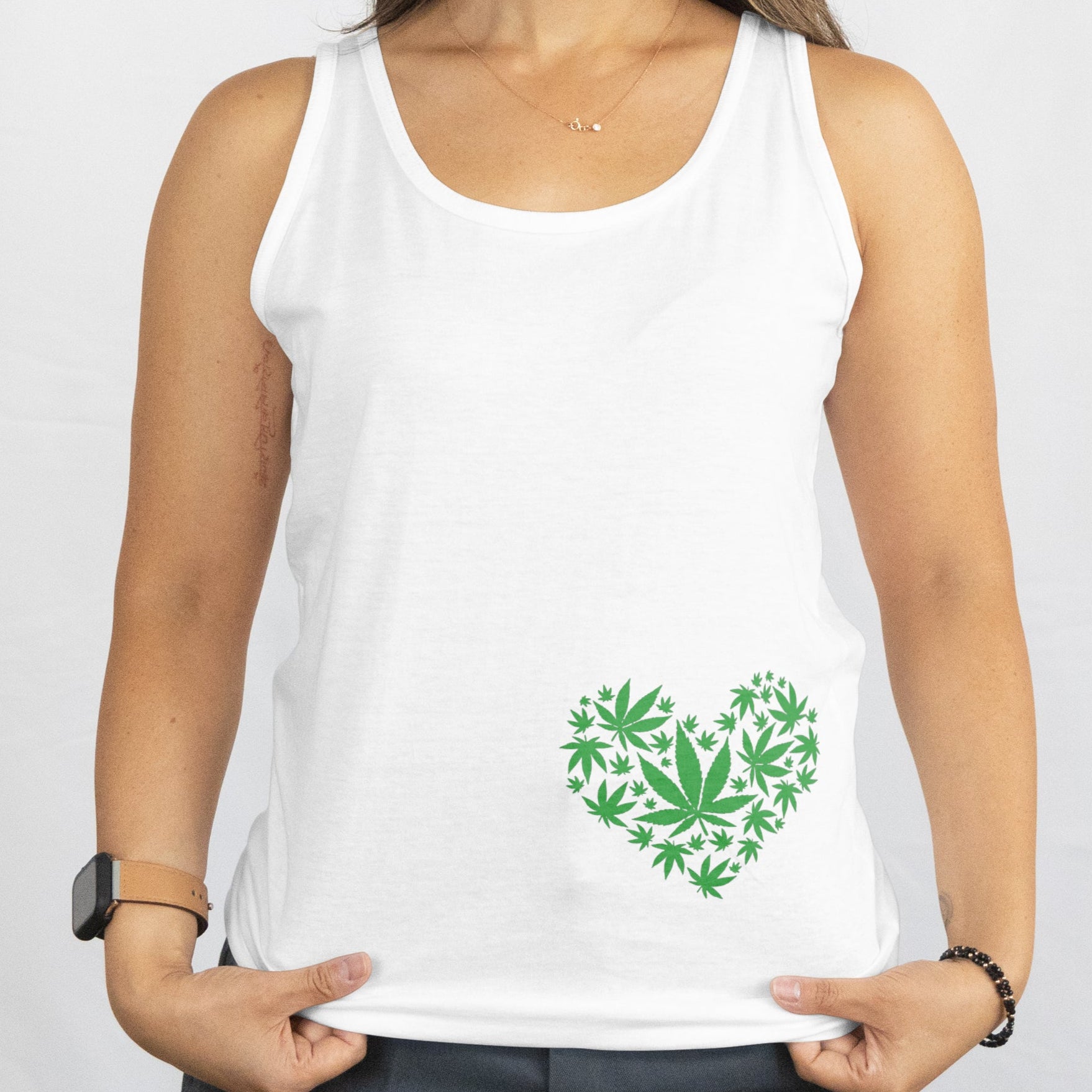 Woman wearing a white tank top with a green heart design on a plain background