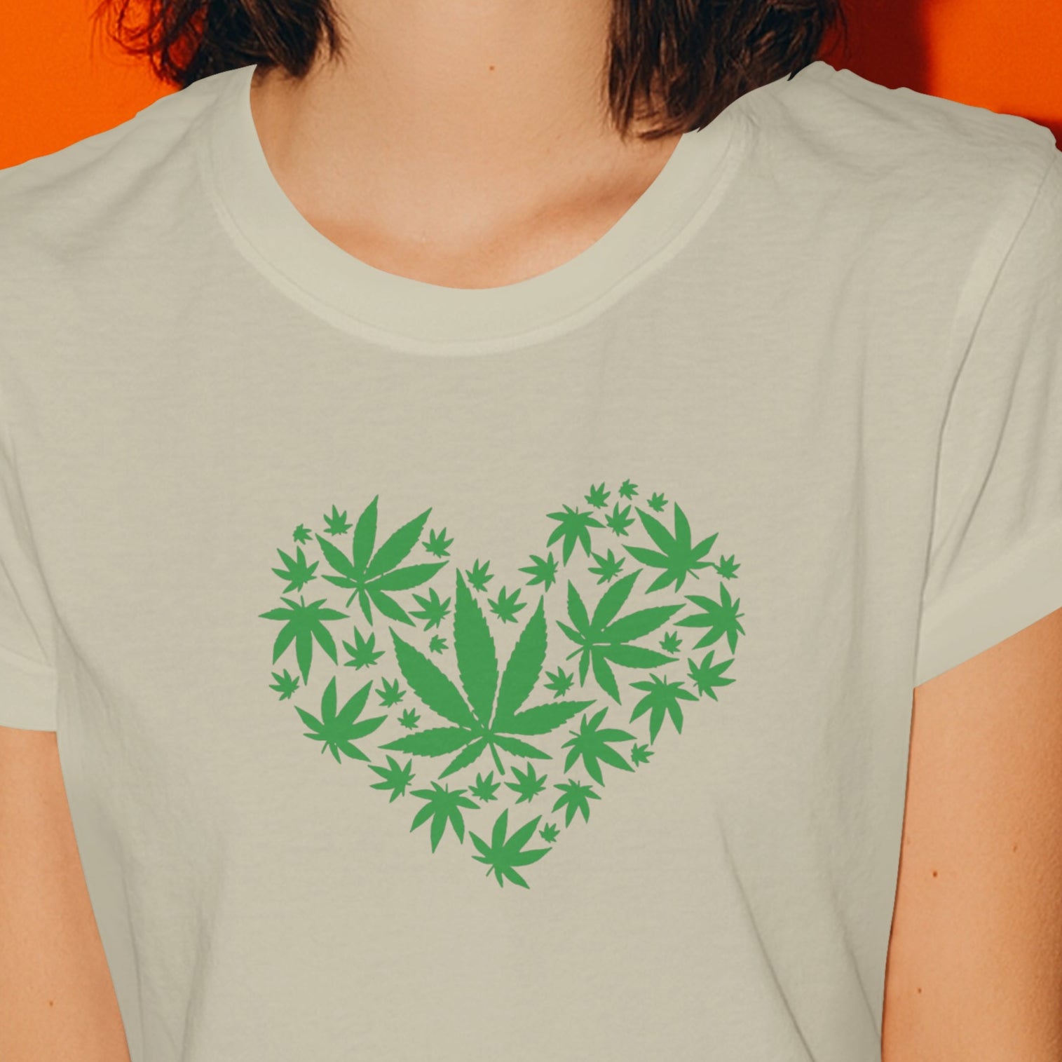 Woman wearing a t-shirt with a heart design made of cannabis leaves against an orange background