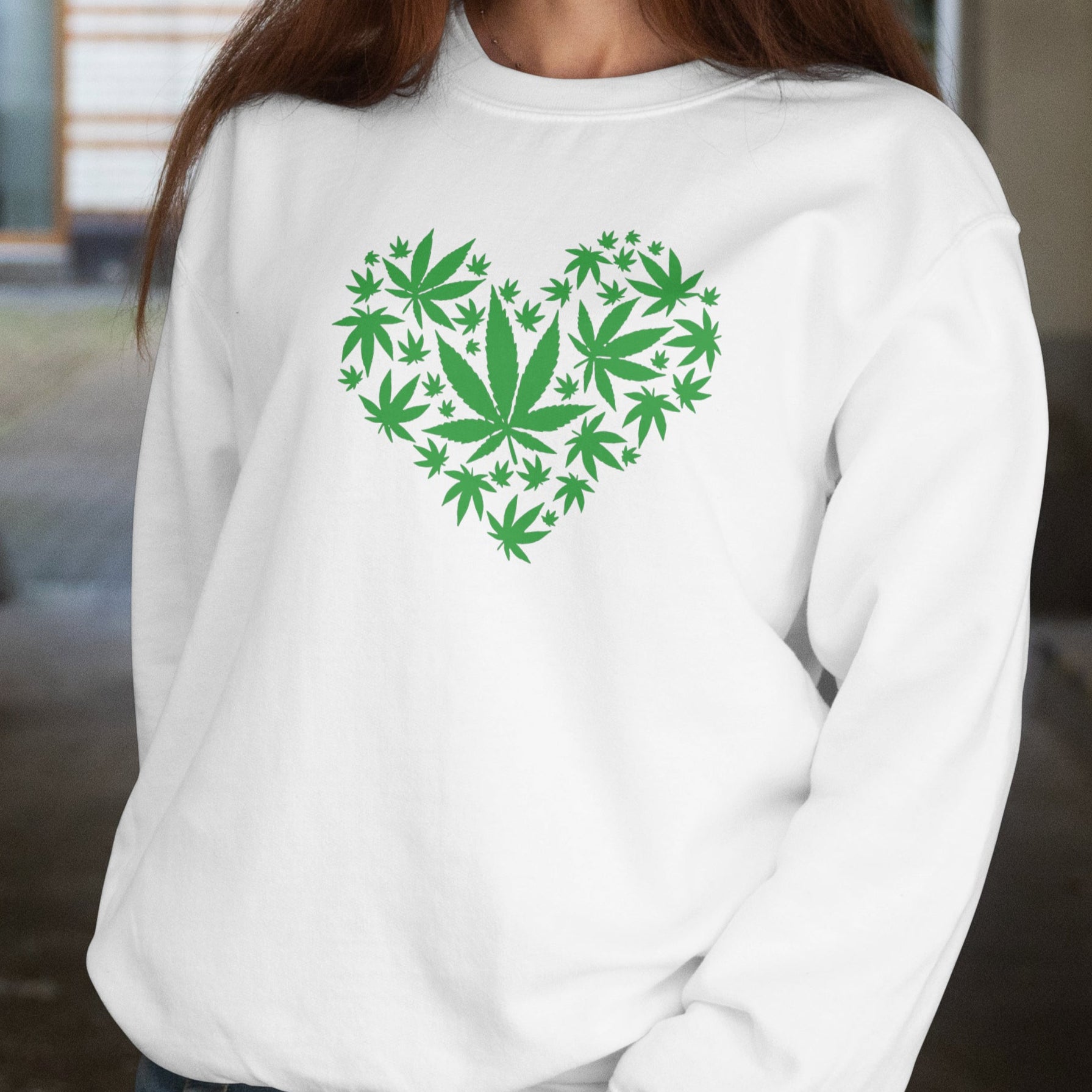 Woman wearing a white sweatshirt with a green cannabis leaf heart design.