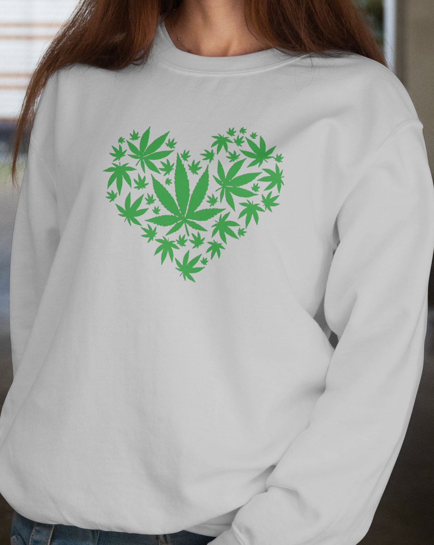 Woman wearing a white sweatshirt with a green heart-shaped design of leaves, standing in a doorway.
