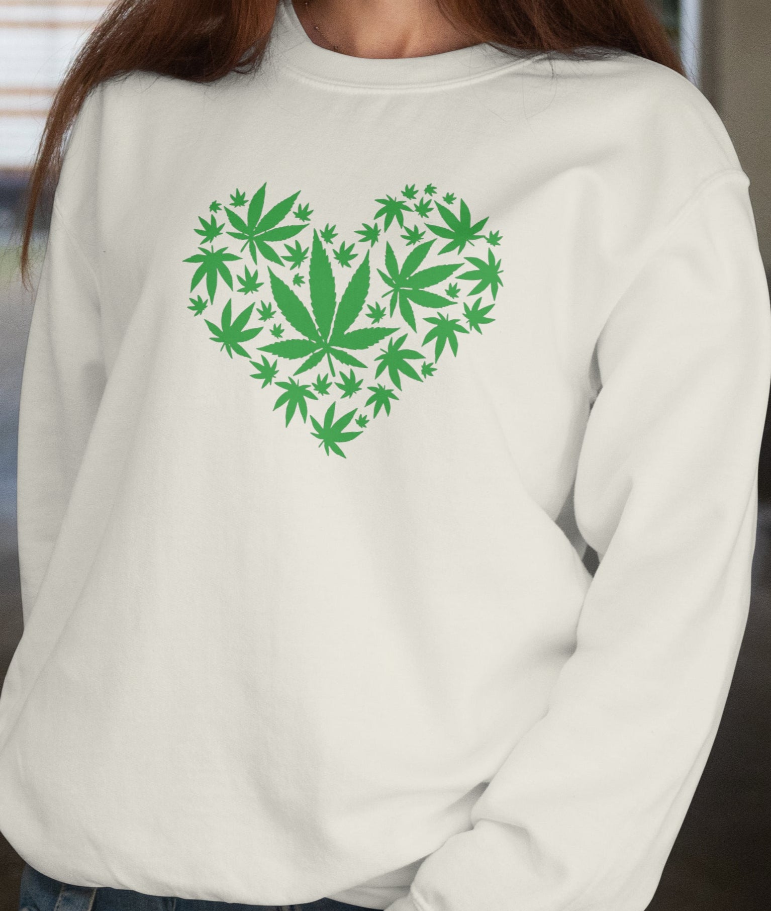 Woman wearing a white sweatshirt with a green heart design made of leaf shapes.