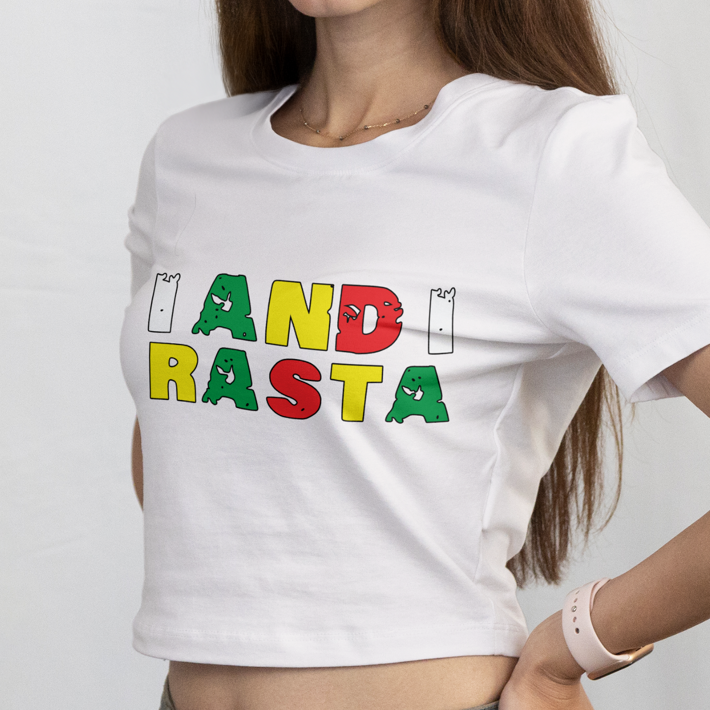 Woman wearing a white t-shirt with 'I ANDI RASTA' text in colorful letters on a plain background