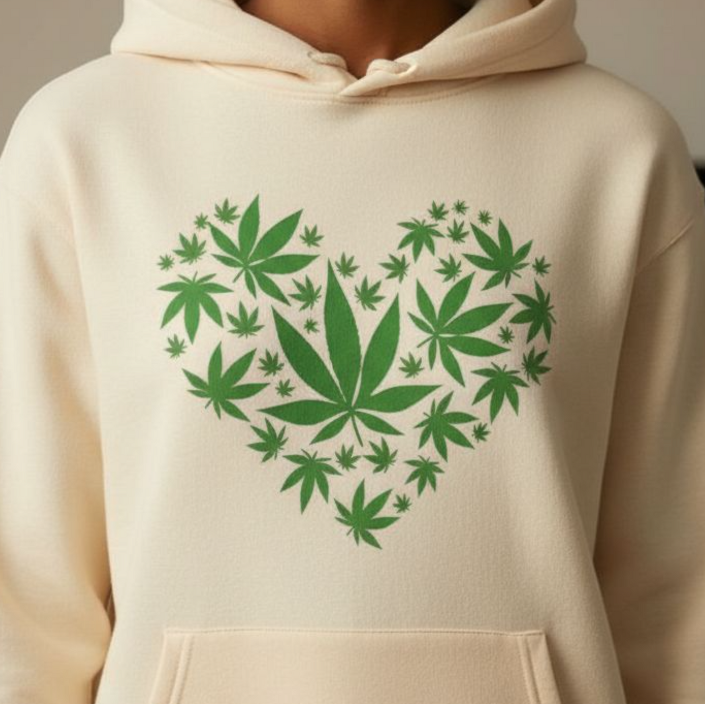 Beige hoodie with green cannabis leaf heart design worn by a person.